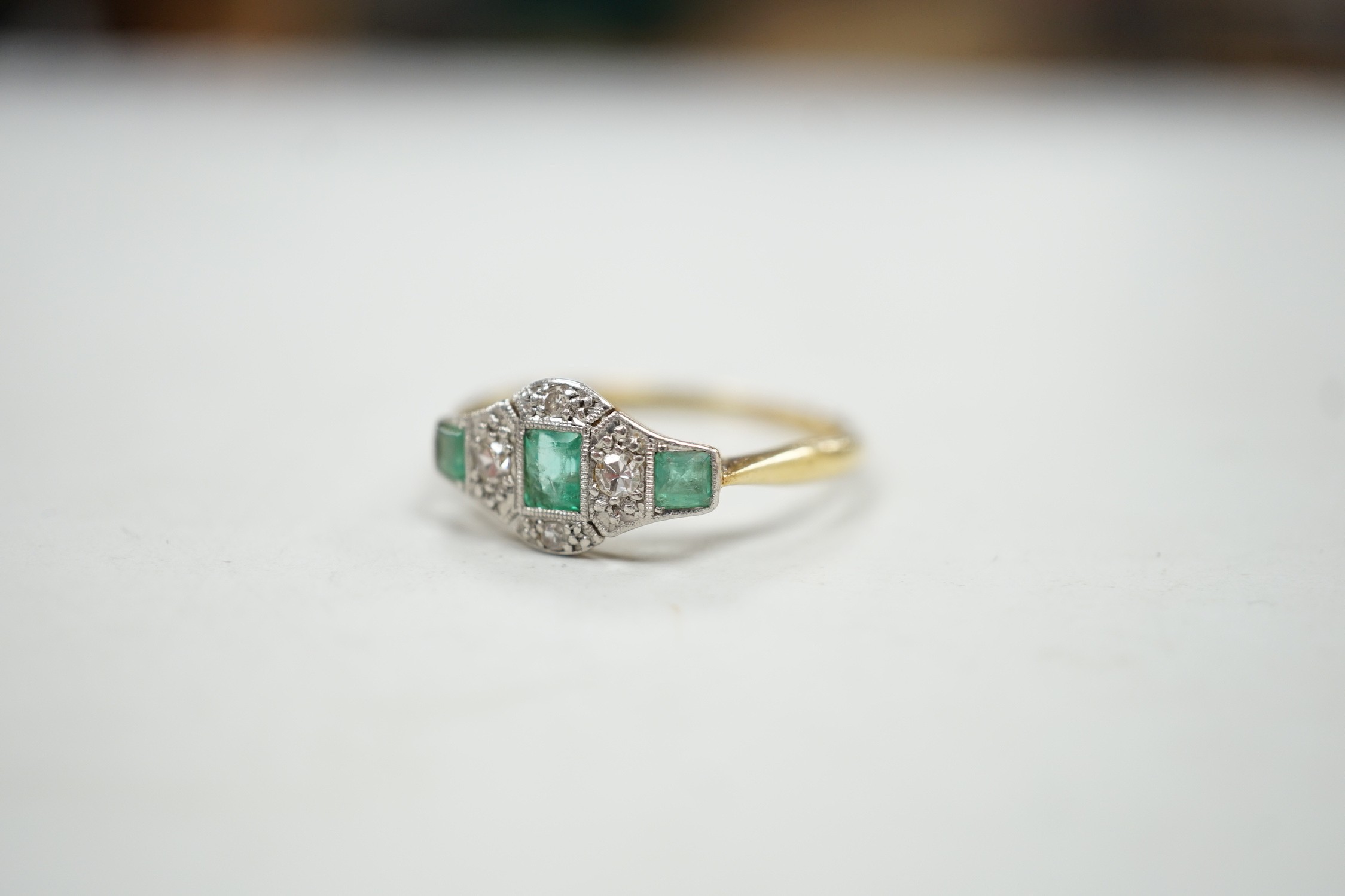 A 1920's 18ct & plat, millegrain set three stone emerald and four stone diamond ring, size R/S, gross weight 2.5 grams.